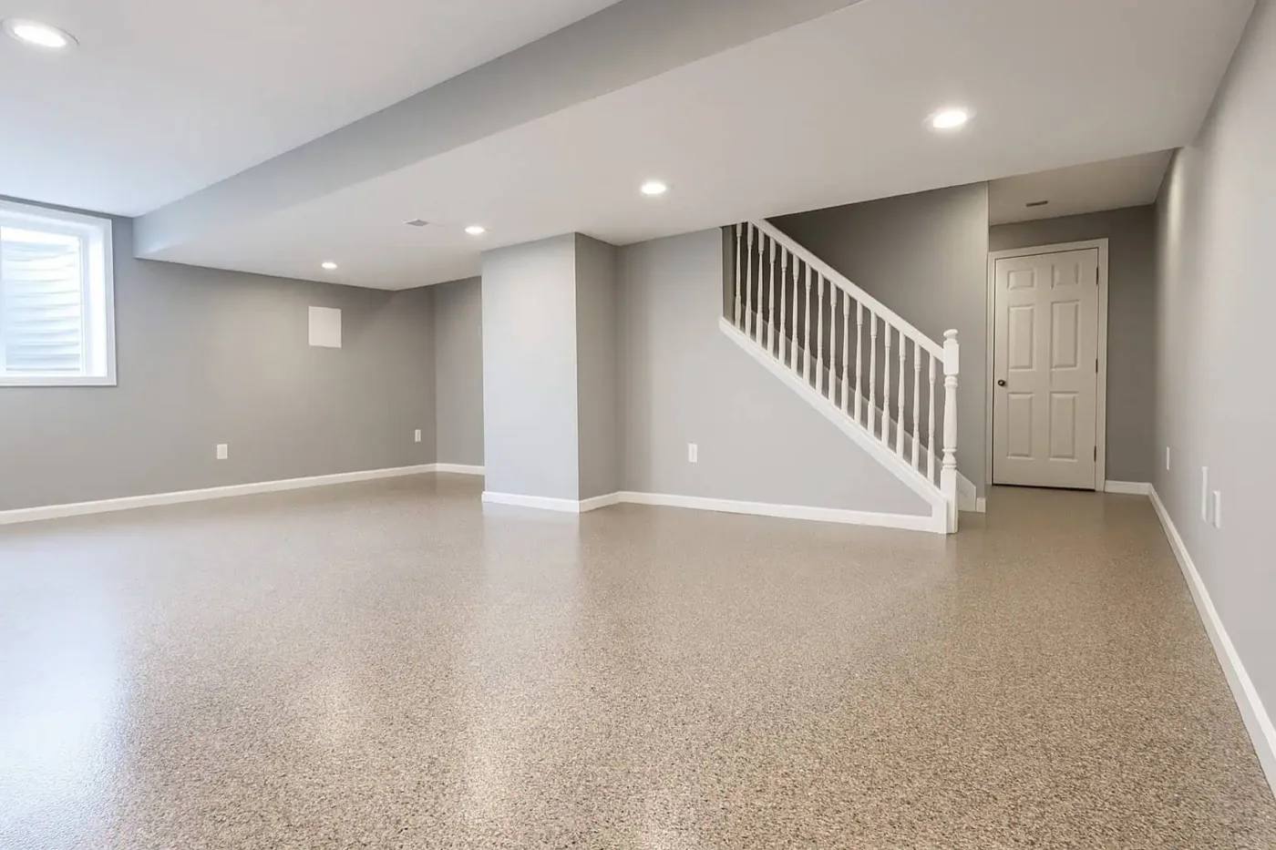 Finished basement floor coated with tan flake epoxy beside a white staircase