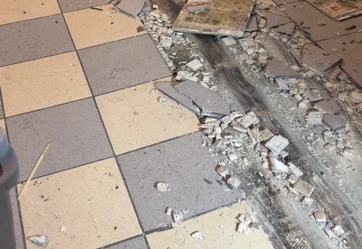 Ride-on scraper lane cut through a ceramic tile floor, broken tile and thinset left in the channel