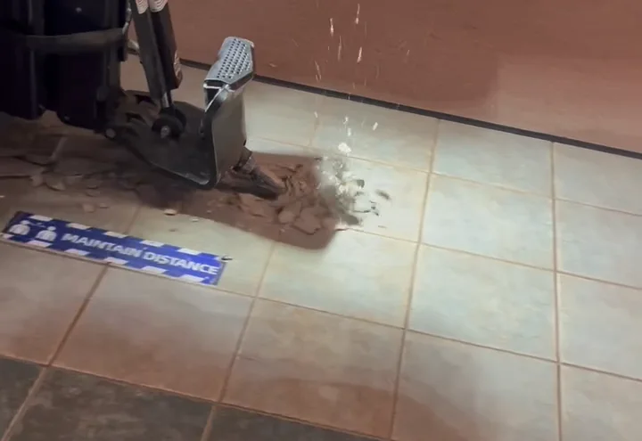 Ride-on scraper blade breaking ceramic tile loose from a commercial floor