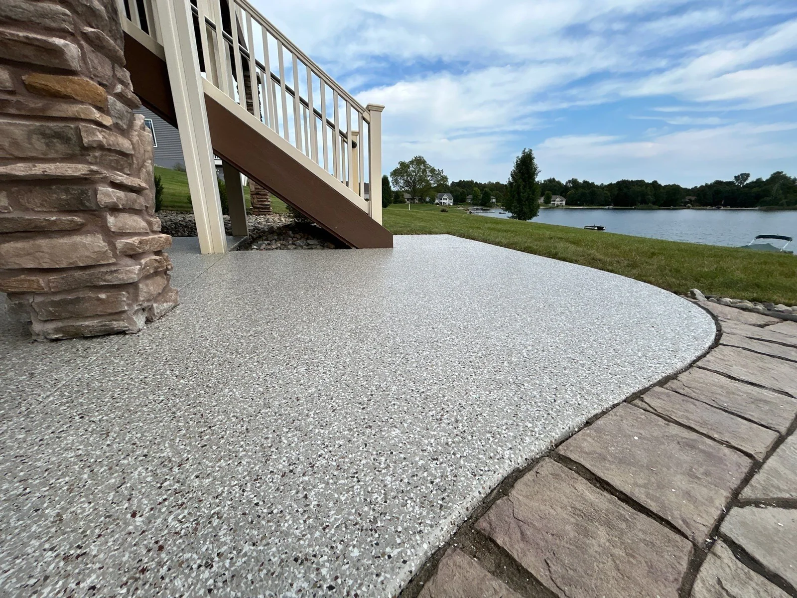 Gray flake epoxy coating on a lakeside concrete patio beside wooden deck stairs
